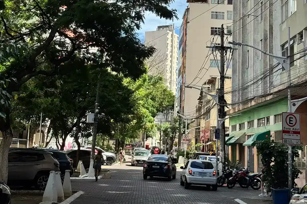 Rua arborizada com carros estacionados e prédios comerciais no Bairro 2 de Julho em Salvador.